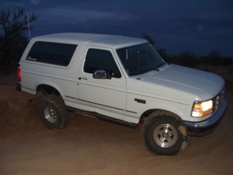 1993 Ford Bronco - White 1993 Ford Bronco with aftermarket wheels and tires sits on a dirt lot.