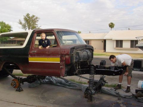 1979 Ford Bronco - A man works on a disassembled Ford Bronco while a child sits in the driver's seat.