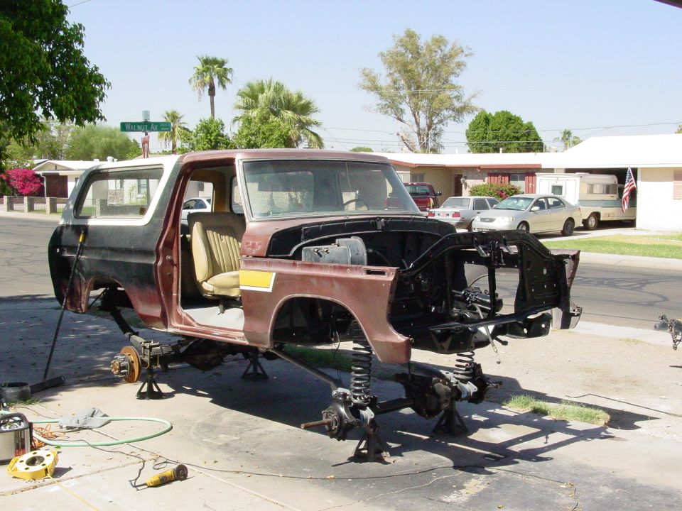 Brown and white Ford Bronco body on jack stands, front end removed, interior visible