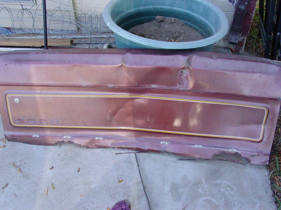 Damaged maroon car door panel with gold trim and visible rust along the bottom edge