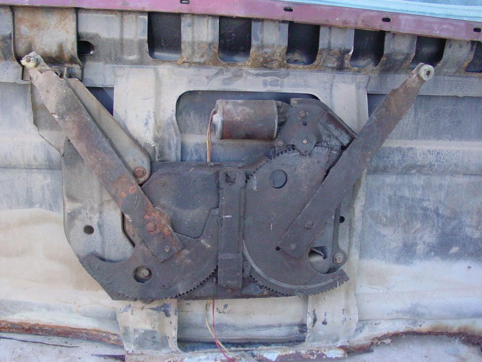 Rusty window regulator mechanism with motor and gears, attached to a red vehicle door interior