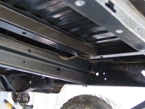 1979 Ford Bronco - The undercarriage of a vehicle shows heavy-duty frame rails and crossmembers, with a tire visible at the bottom.