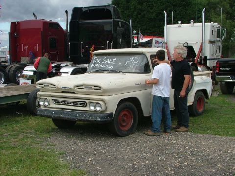 2001 Ford Fiesta - A weathered pickup truck is parked outside with two men inspecting it, while large semi-trucks are visible in the background.