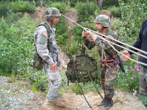 2003 Jeep TJ - Two soldiers prepare to move a heavy backpack using ropes in a wooded outdoor environment.
