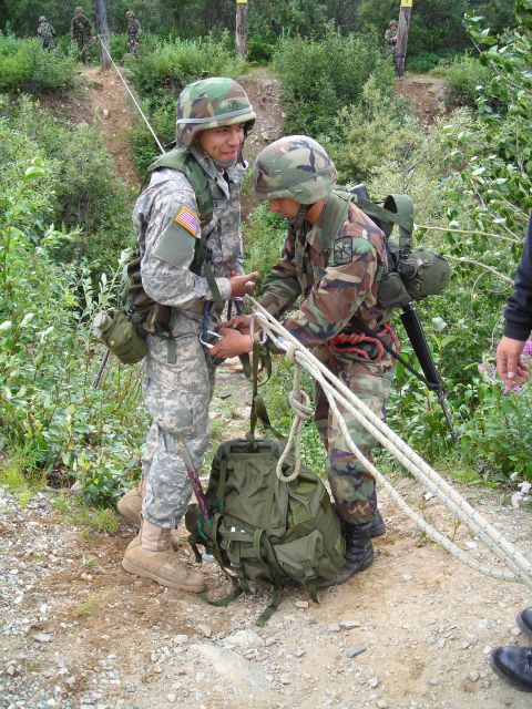 2003 Jeep TJ - Two soldiers are seen interacting with ropes and backpacks during an outdoor training scenario, possibly for rappelling or climbing.
