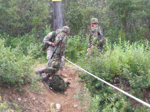 2003 Jeep TJ - Soldiers are seen navigating a challenging terrain with the assistance of a rope.