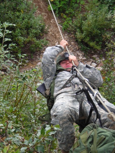 2003 Jeep TJ - A soldier in camouflage fatigues rappels down a steep, wooded incline, holding onto a rope for support.