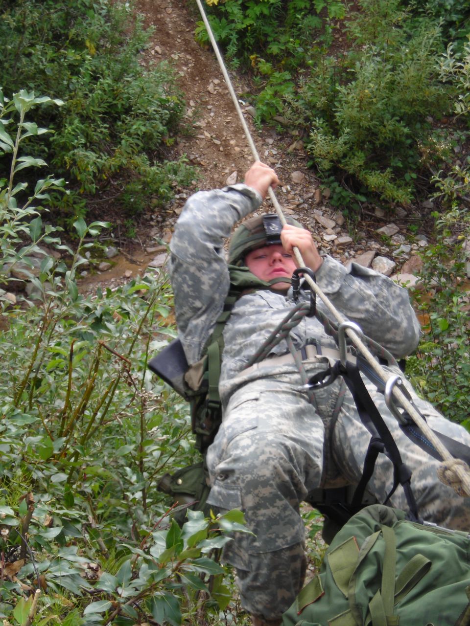 Soldier rappelling down a wooded slope using a rope