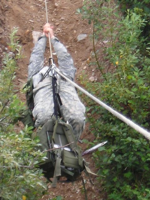 2003 Jeep TJ - A soldier is rappelling down a steep, wooded slope using a rope and harness.