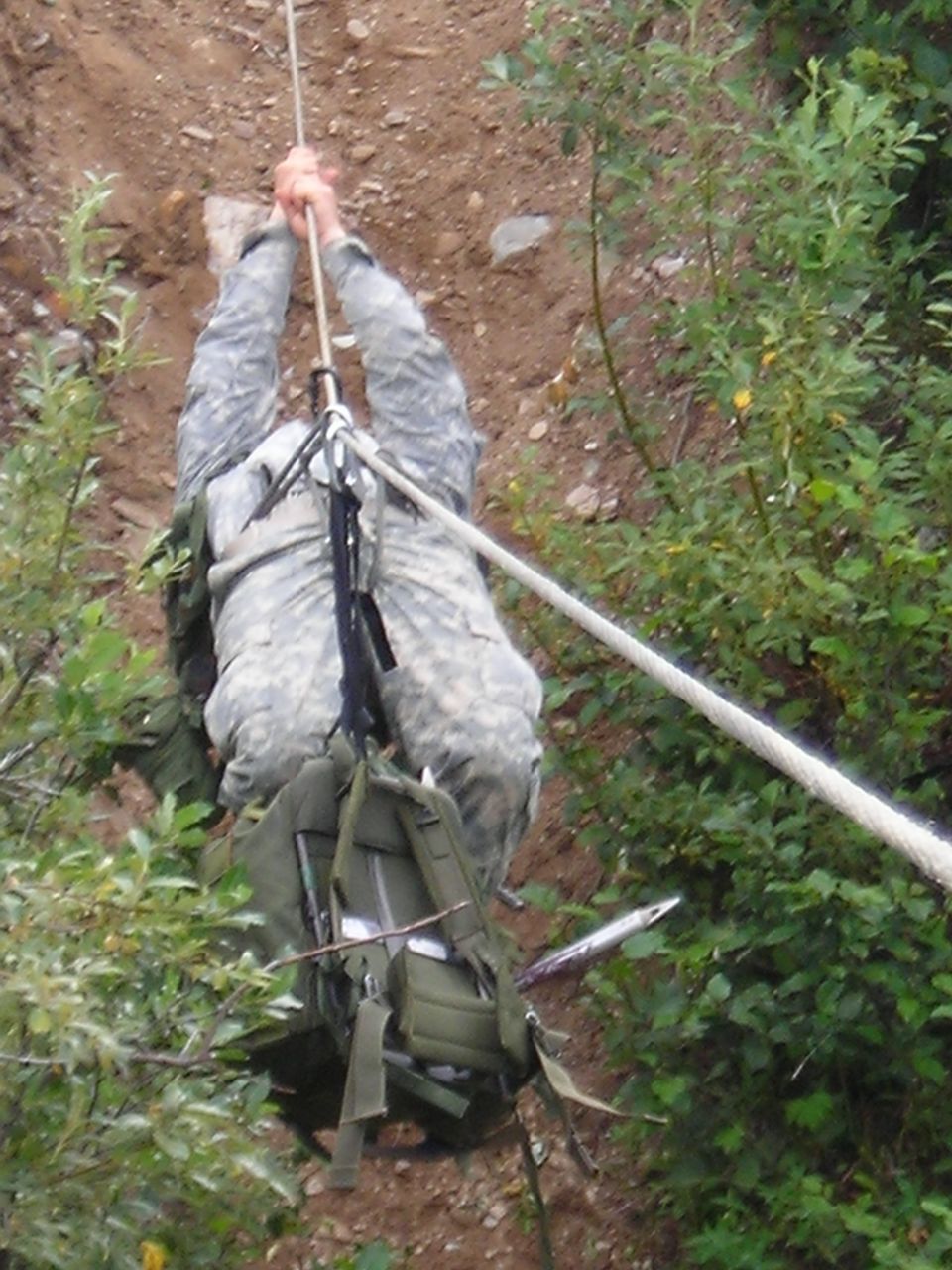Soldier in camouflage rappelling down a dirt embankment with a backpack