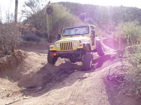 1993 Ford Bronco - A yellow Jeep Wrangler navigates a dusty, off-road trail in a desert environment.