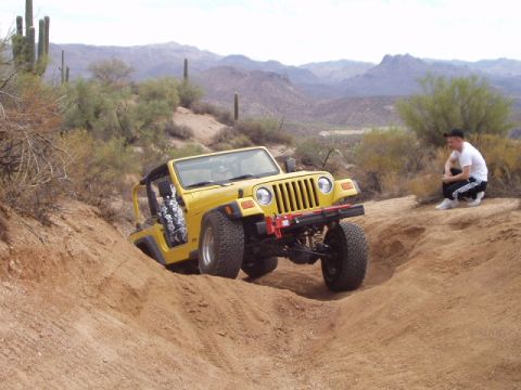 1993 Ford Bronco - Yellow Jeep Wrangler navigates a steep dirt incline in a desert environment.