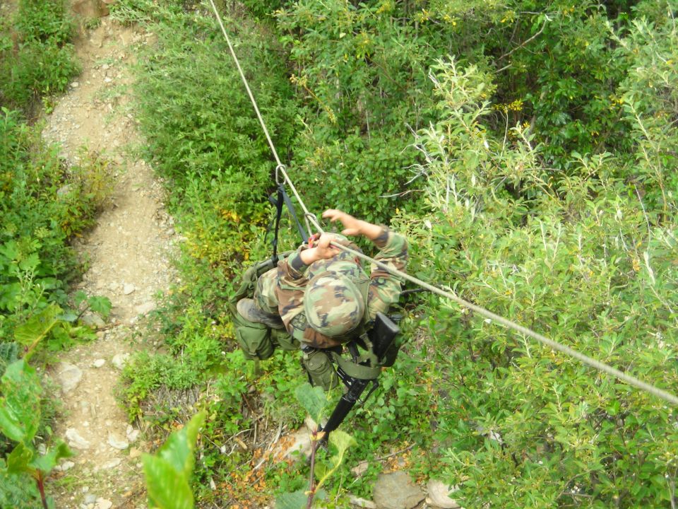Soldier in camouflage rappelling down a rocky, overgrown path