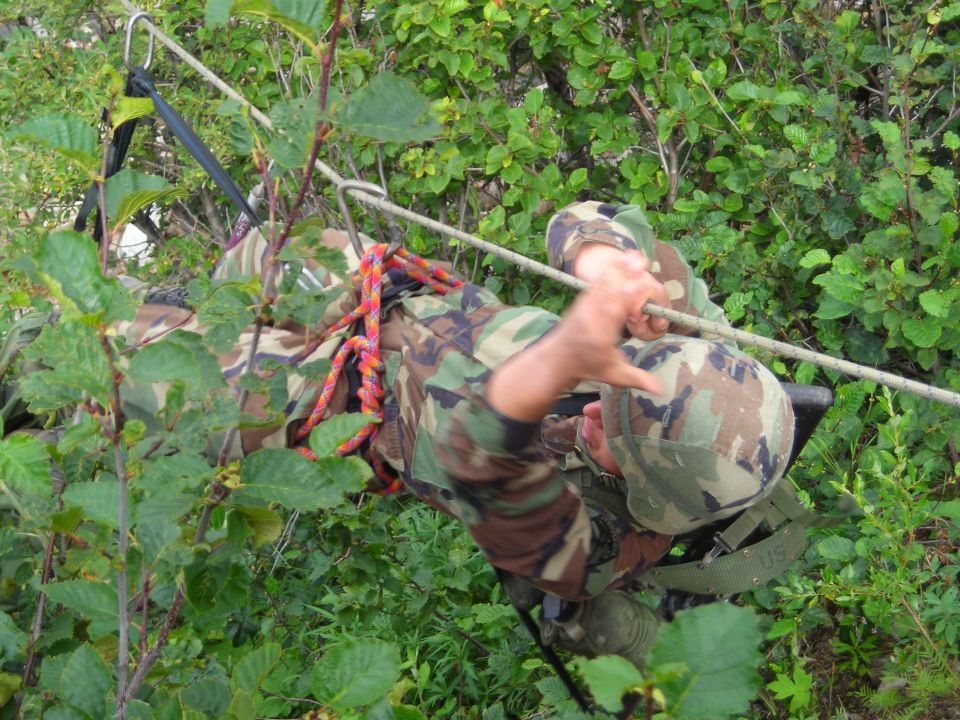 Soldiers in camouflage rappelling down a slope with ropes and gear