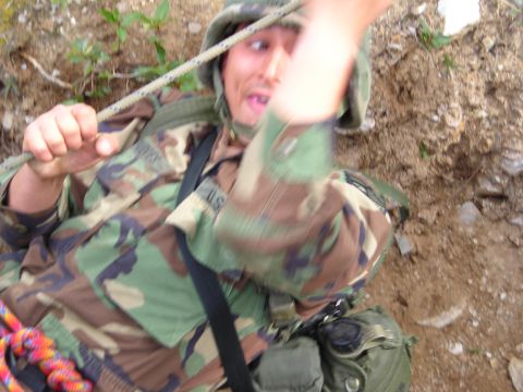 2003 Jeep TJ - Soldier in camouflage uniform and helmet is rappelling down a dirt embankment while holding a rope.