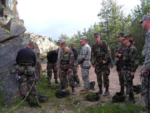 2003 Jeep TJ - Military personnel in camouflage uniforms are gathered outdoors near a large rock formation, appearing to prepare for a climbing activity.
