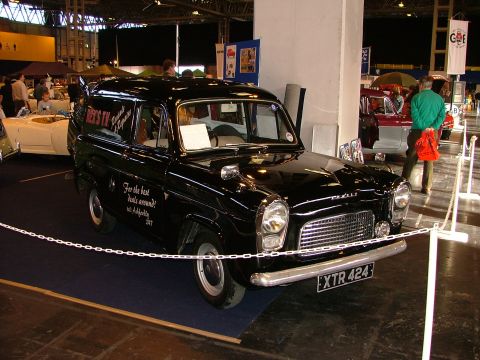 2001 Ford Fiesta - A vintage black van, possibly a Ford Anglia, is displayed indoors with text on its side.