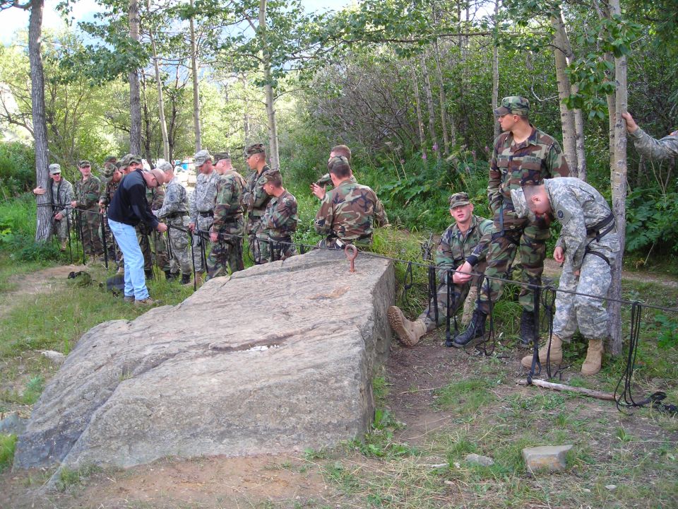 Military personnel gathered around a large rock outdoors