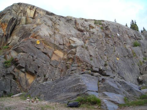 2003 Jeep TJ - A large rock face with visible climbing routes and markers, with a bag at its base.