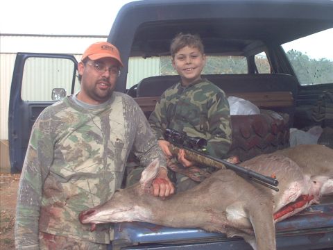 1985 Ford Bronco - Two hunters pose with their successful hunt, a deer laid out on the tailgate of a truck.