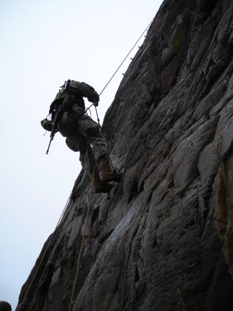 2003 Jeep TJ - A soldier practices rappelling down a steep rock formation against an overcast sky.