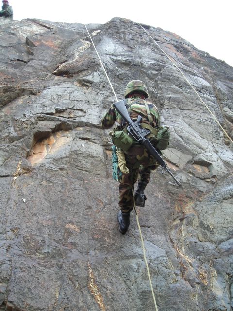 2003 Jeep TJ - A soldier in camouflage rappels down a steep rock face, carrying a rifle and equipment.