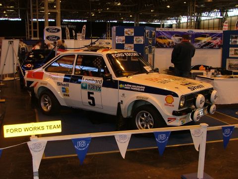 2001 Ford Fiesta - A white Ford Escort rally car with "Lombard Rally" livery is displayed at an indoor event.