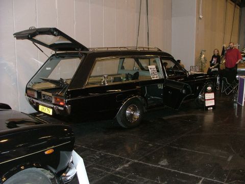 2001 Ford Fiesta - A black hearse is displayed with its rear hatch and side doors open, showing its interior. Another black vehicle is partially visible in th…