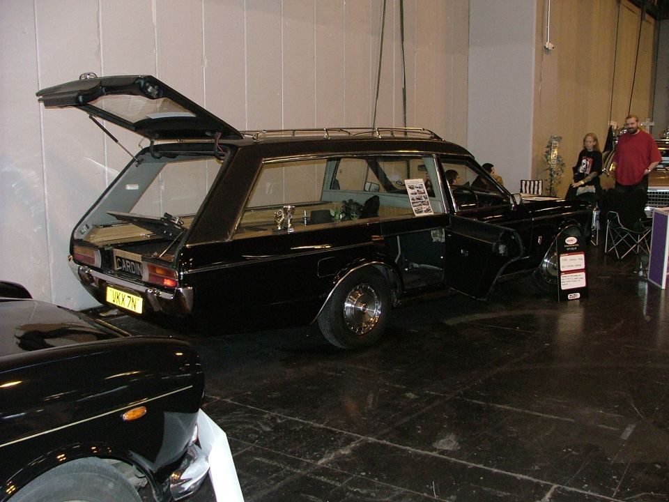 Black hearse, rear and side doors open. UKK 7N license plate