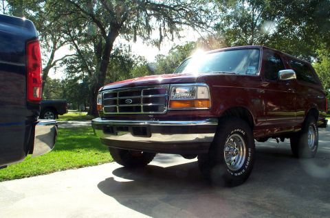 1996 Ford Bronco - A maroon Ford Bronco is parked on a driveway, with a dark pickup truck to its left.