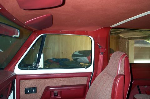1996 Ford Bronco - The interior of a red vehicle features patterned seats and door panels, with red sun visors visible on the headliner.
