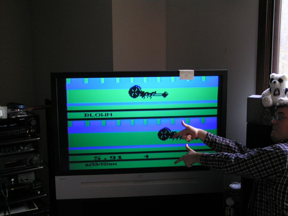 TV showing Activision Dragster game screen reading BLOWN and 5.91 as a person points at it
