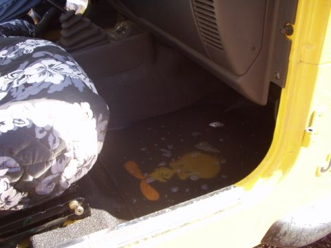 1993 Ford Bronco - Interior view of a yellow vehicle with a patterned seat cover and a cartoon on the floor mat.
