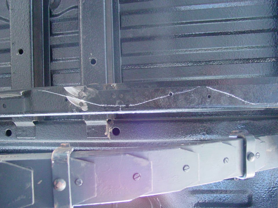 Close-up of vehicle frame rails and leaf spring assembly. White chalk marks are visible on the frame