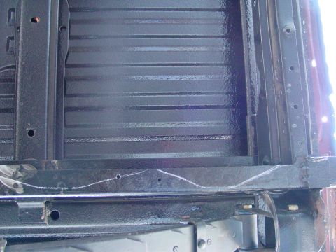 1979 Ford Bronco - The underside of a truck bed shows a ribbed surface with black protective coating and chalk markings.
