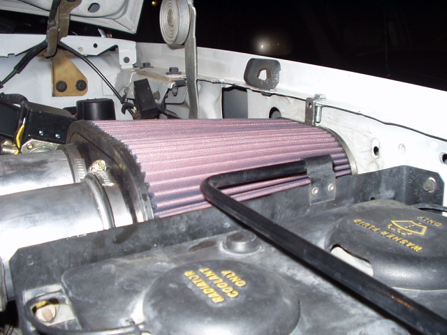 Engine bay close-up of a red K&N style cone air filter and rubber intake tube
