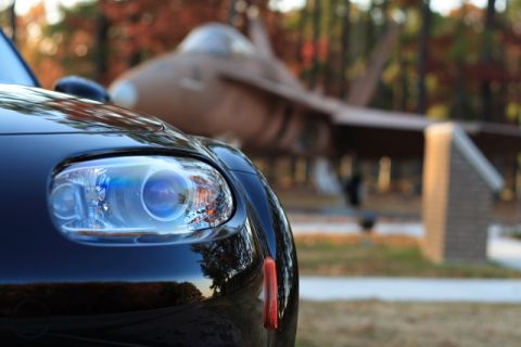 2006 Mazda Miata - A black 2006 Mazda Miata is parked in front of an airplane.