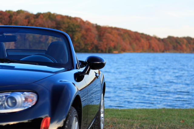 Black 2006 Mazda Miata convertible parked by a lake with fall foliage