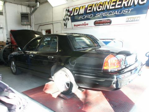 2001 Mercury Grand Marquis - A black sedan is positioned on a dynamometer inside a garage with the hood up and a number on the window.