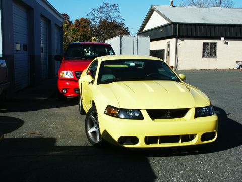 2001 Mercury Grand Marquis - A yellow Ford Mustang is parked in front of a red Ford F-150 outside a building.