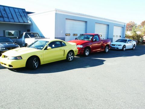 2001 Mercury Grand Marquis - A line of vehicles, including a yellow 2001 Ford Mustang coupe, a red pickup truck, and a white coupe, are parked outside a garage.