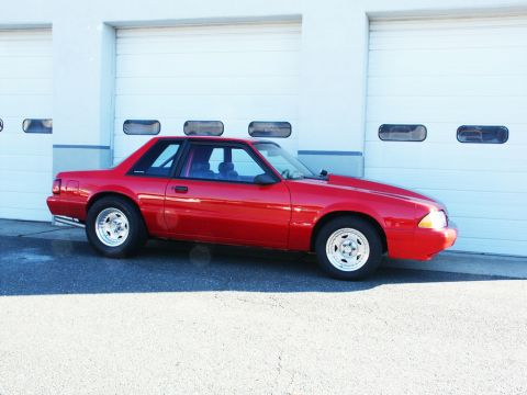 2001 Mercury Grand Marquis - Side view of a red coupe with a modified hood, parked outside a building with garage doors.