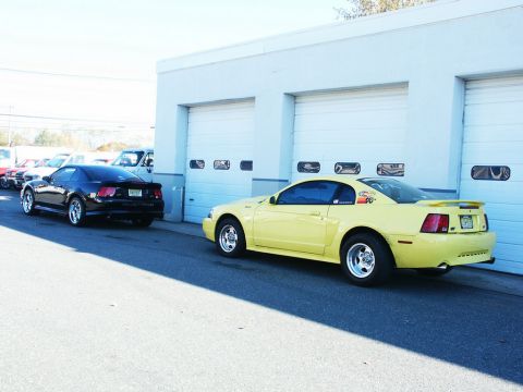 2001 Mercury Grand Marquis - Two Mustangs are parked outside a building with multiple garage bays on a sunny day.
