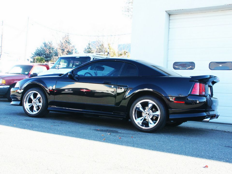 Black coupe with spoiler and chrome wheels, 3q-front view. Other vehicles visible
