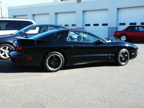 2001 Mercury Grand Marquis - Side view of a black Pontiac Firebird parked outdoors with other vehicles nearby.