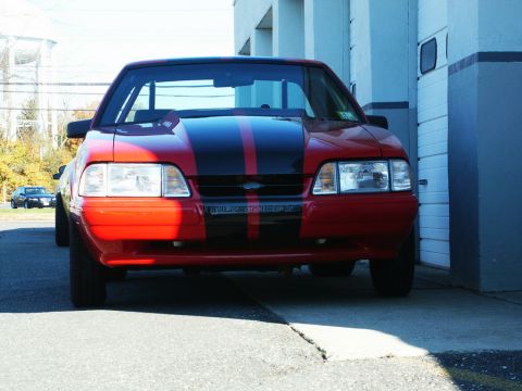 2001 Mercury Grand Marquis - Front view of a red Ford Mustang with black racing stripes, parked outdoors.