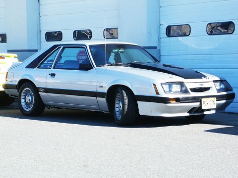 2001 Mercury Grand Marquis - A 1985 Ford Mustang GT is parked in front of a garage door.