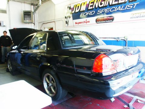 2001 Mercury Grand Marquis - A black sedan is positioned on a dynamometer in a garage with a "JDM Engineering Ford Specialist" banner in the background.
