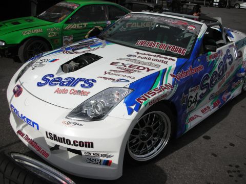 1998 Ford Crown Victoria - white and blue drift car wearing Nissan and Sears Auto Center livery with number 64 sits in a paddock.