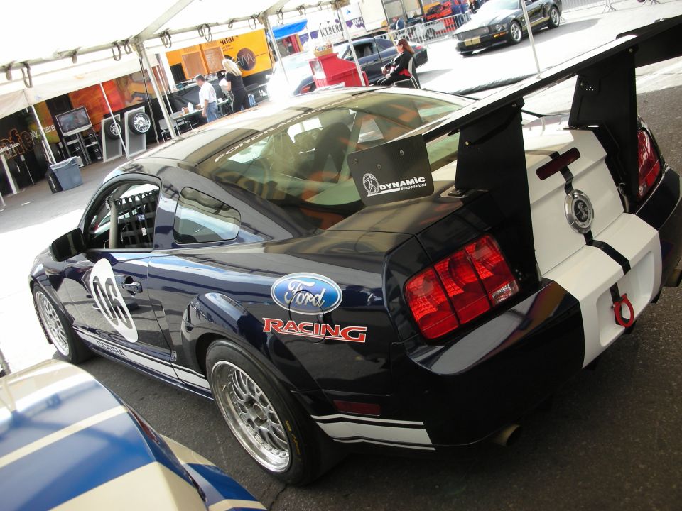 Dark blue Ford Racing Mustang with white stripes and tall rear wing, rear three-quarter view
